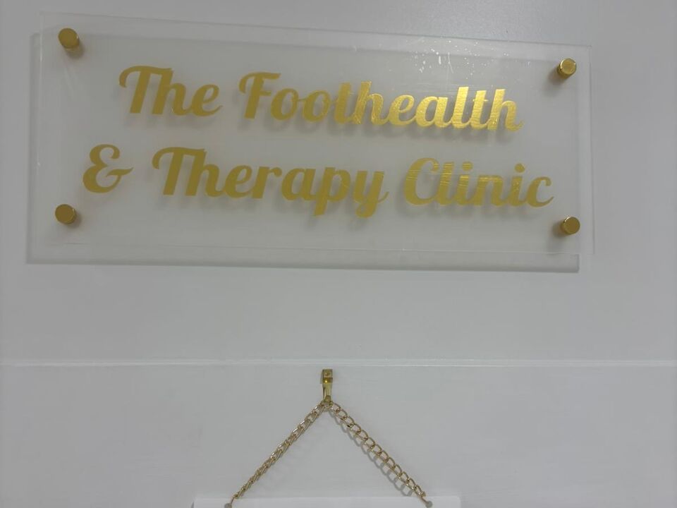 The clinic's frosted glass sign in gold lettering, The Foothealth and Therapy Clinic, mounted on the treatment room wall