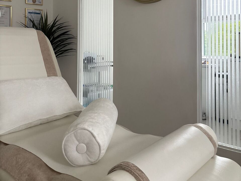 The reflexology couch made up with rolled bolster cushions and a folded towel, beside the clinic window