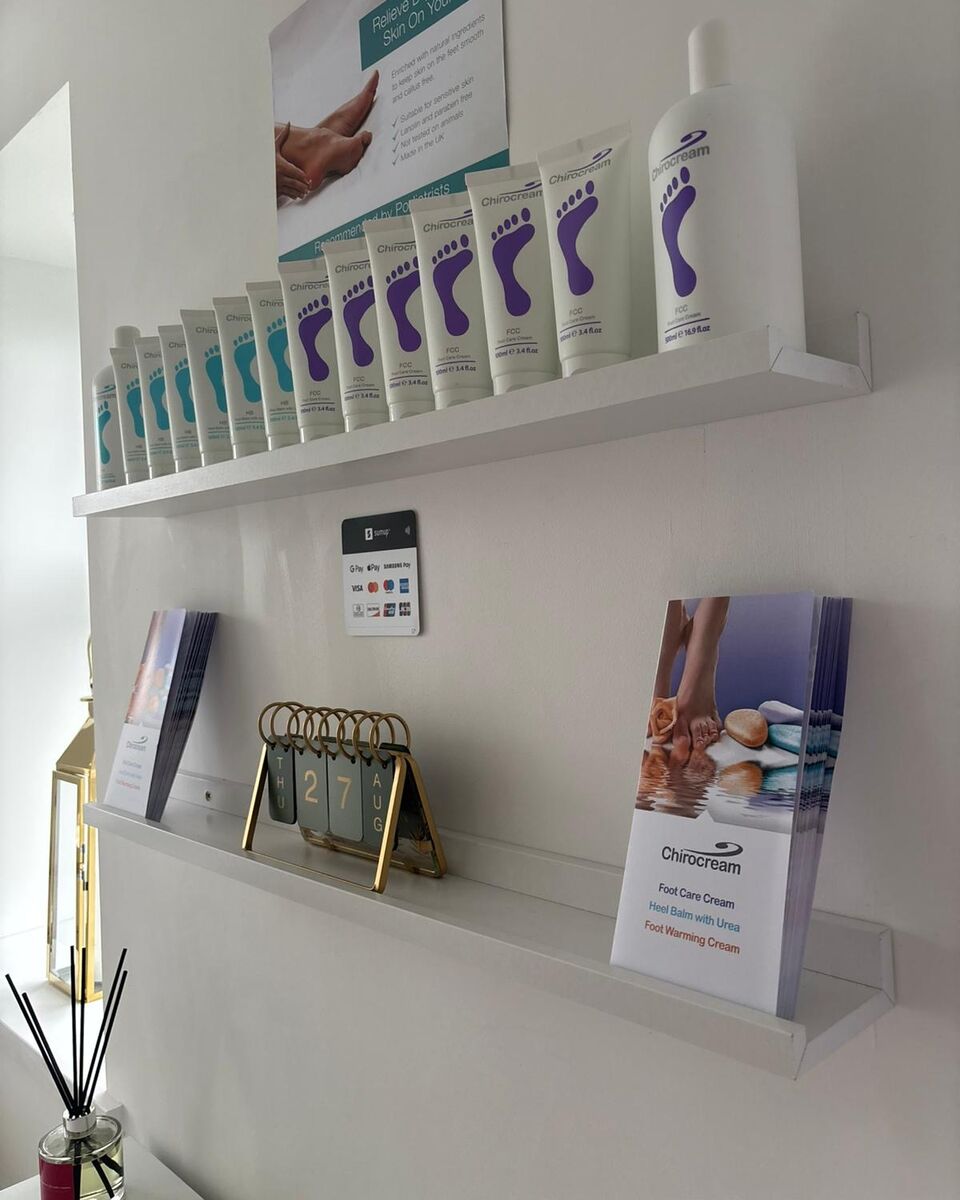 A shelf of Chirocream foot care creams and lotions in the clinic, with product leaflets and an appointment card holder on the shelf below