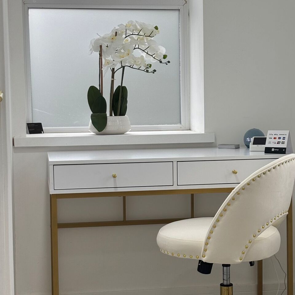 The clinic reception, with a white orchid on the windowsill, a white and gold desk, a studded cream chair and a card machine